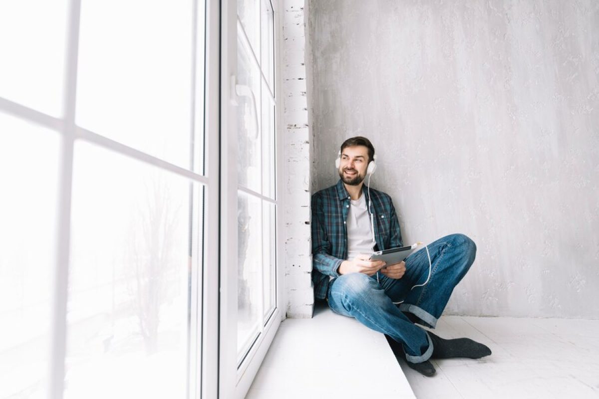 cheerful-man-listening-music-looking-out-window_23-2147800055